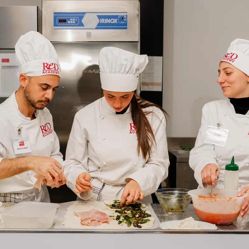 Tre allievi farciscono le focacce in teglia al banco in acciaio