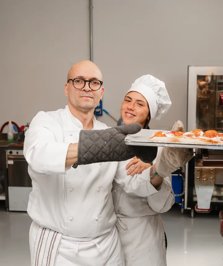 Docente con il guanto da forno e allieva con una teglia appena sfornata