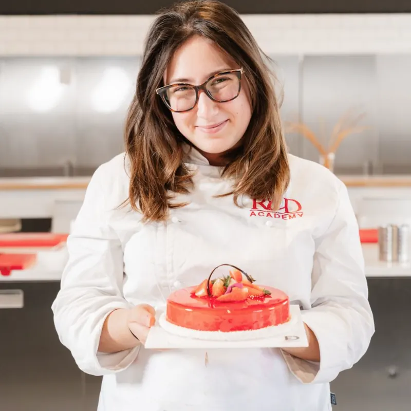Allieva del corso di pasticceria con la torta dalla glassa rossa e fragole