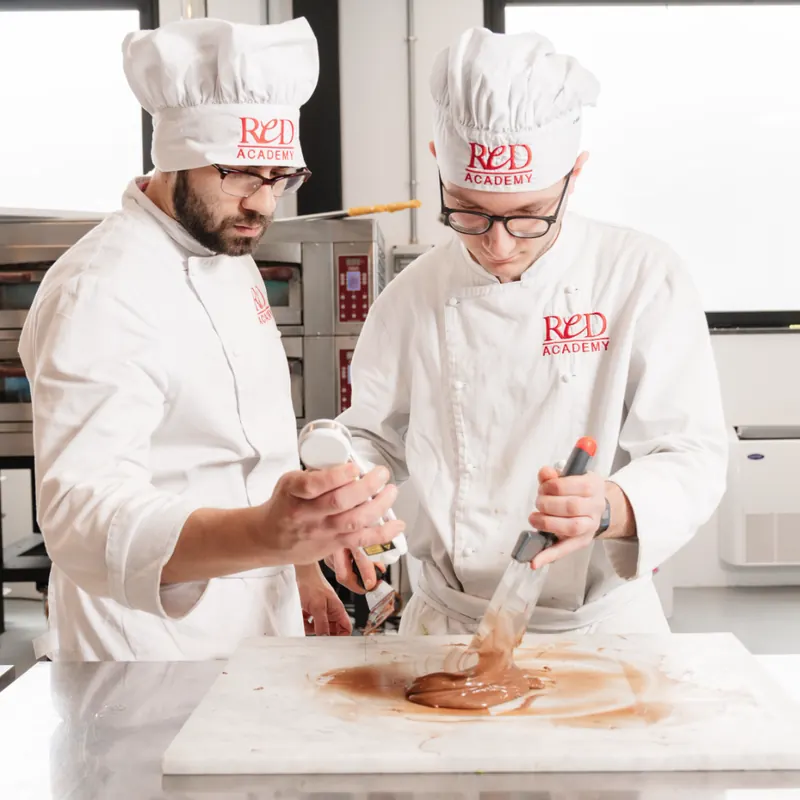 Due allievi temperano il cioccolato sul piano di marmo