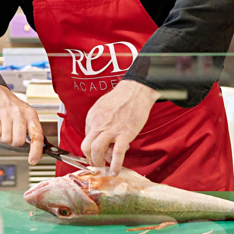 chef con grembiule rosso sfiletta un pesce intero