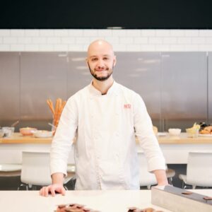 Cristopher pelosi resident chef conngiacca bianca con logo red in rosso in cucina