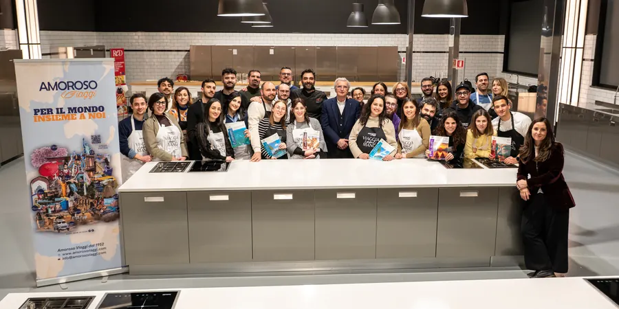 Foto di gruppo del team di Amoroso Viaggi nell'aula di cucina di ReD, con i cataloghi delle mete