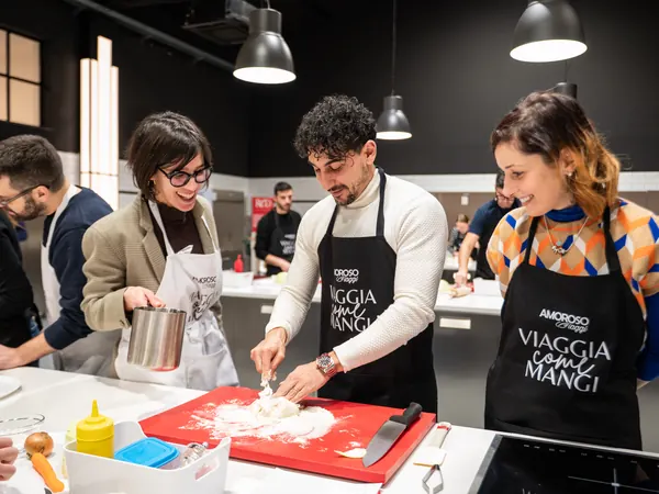 Tre partecipanti lavorano un impasto sul tagliere rosso